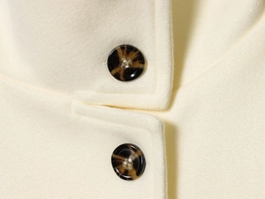 Macro view of cream white double-sided wool coat featuring tortoiseshell buttons and fine stitching