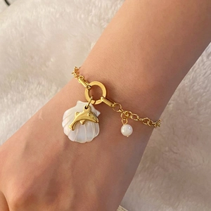 Golden stainless steel bracelet with shell, dolphin and pearl charms on model's wrist