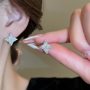Sparkling silver star stud earrings with clear gemstones worn on model ear and hand