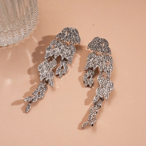Macro view of long silver drop earrings with crystal leaf tassels on a warm background