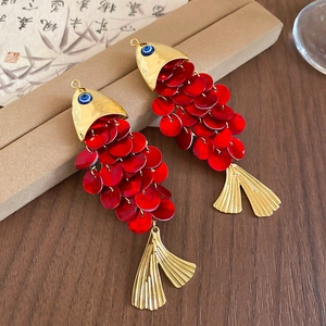 Macro detail of fish shaped hair clips with red scales and evil eye design on wood background