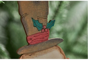 Macro detail of hand-painted wooden snowman ornament with red scarf and holly leaf