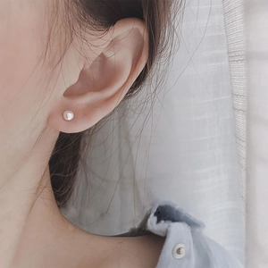 Close-up of a minimalist round pearl stud earring worn on the earlobe with a soft white glow