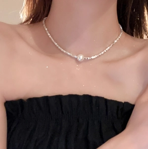 Detailed view of silver metallic chain necklace with a single round pearl on neck