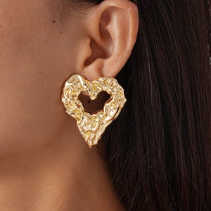 Close-up of a large vintage gold heart earring with lava texture worn by a model