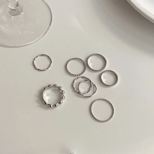 Set of eight silver minimalist rings featuring wave and bead designs on a white surface