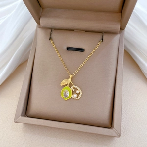 Macro detail of a gold lemon pendant necklace with green enamel and pearl accents