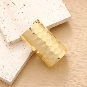 Macro shot of minimalist gold cuff bracelet with honeycomb hammer texture on stone surface