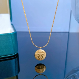 Détail d'un collier en acier titane doré avec pendentif symbole double bonheur