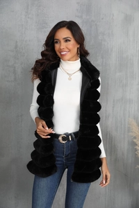 Détail de la veste longue en fausse fourrure noire sur un pull blanc pour femmes