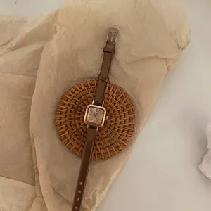 Retro small square women's watch with gold case and brown leather strap on vintage paper