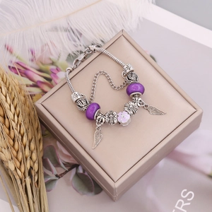 DIY charm bracelet with purple beads and angel wing pendant on a jewelry display box