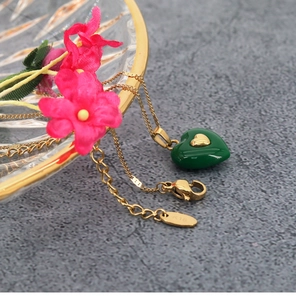 Macro shot of K18 gold necklace with green heart pendant and engraved metal hallmark tag