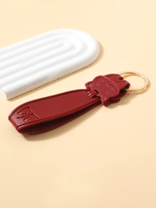 Macro detail of red leather cat-shaped keychain with gold-tone metal ring on beige backdrop