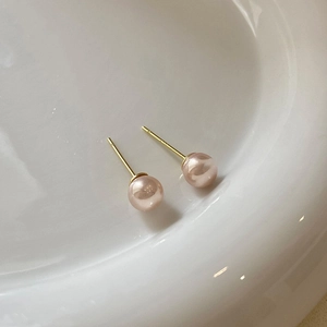 Close-up of pink pearl stud earrings with gold needles on a white ceramic plate