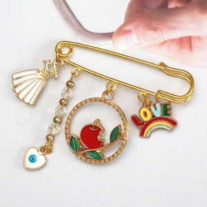 Detail of gold safety pin brooch with enamel evil eye and heart charms on white background