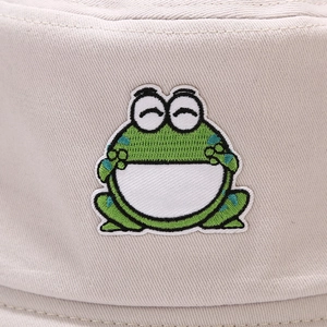 Close-up of a cute green frog embroidery on a beige cotton canvas bucket hat fabric