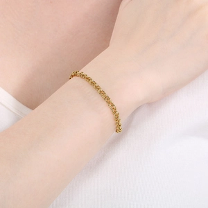 Detailed view of a gold knot chain bracelet worn on a wrist with polished metal finish