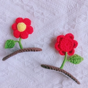 Detail of handmade crochet flower hair clips with red petals and green leaves on lace
