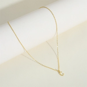 Macro detail of polished 3D initial C pendant on a delicate gold-toned chain necklace