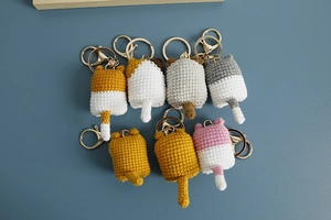Close-up of handmade crochet cat keychains in various colors on a blue surface