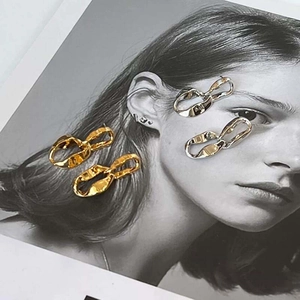 Minimalist twisted metal hoop earrings in gold and silver finish on artistic background