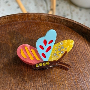 Colorful acetate butterfly hair claw clip with rhinestones shown on a wooden tray