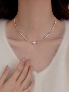 Close-up of a white pearl pendant necklace on a silver chain worn with a white sweater