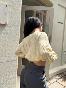 Detailed back view of a light yellow cable-knit sweater with elegant texture on a female model