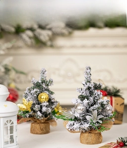 Close-up of mini snow-flocked Christmas trees with gold ornaments and burlap base