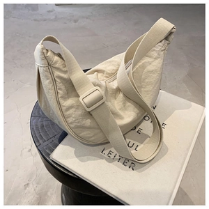 Detail of a minimalist off-white dumpling bag with adjustable wide strap on a table