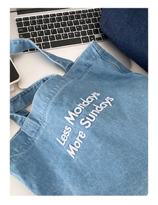 Détail du cabas en denim bleu clair avec broderie blanche à côté d'un ordinateur portable