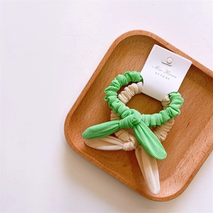 Detail view of two pastel bow hair ties in beige and mint green on a wooden tray
