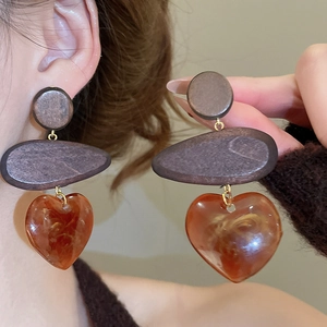 Close-up of vintage heart drop earrings with wood and amber resin on a female model