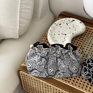 Detail of embroidered paisley evening clutch with large pearl clasp on woven table
