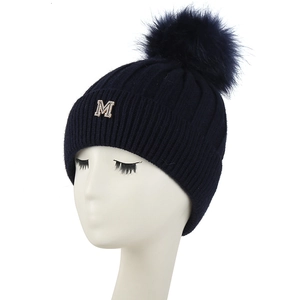 Détail du bonnet en tricot bleu marine avec pompon en fourrure et lettre M en strass