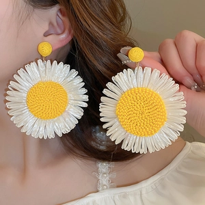 Macro detail of large woven daisy earrings with white petals and yellow core for vacation