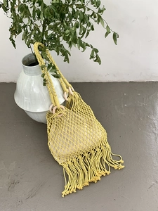 Close-up of yellow hand-woven straw bag with fringe details and round handles for beach