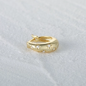 Close-up of gold huggie hoop earring with sparkling zircon star patterns and hinged clasp