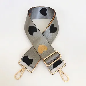 Close-up of gray nylon bag strap with heart patterns and gold-tone metal hooks