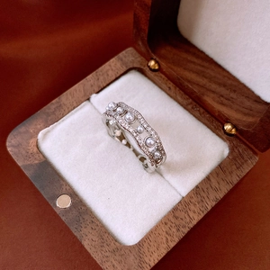 Detail of a wavy silver ring with white pearls and micro-pave zircons in a wooden box