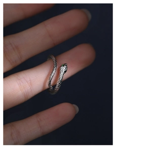 Macro view of a silver snake ring featuring green gemstone eyes on a female finger
