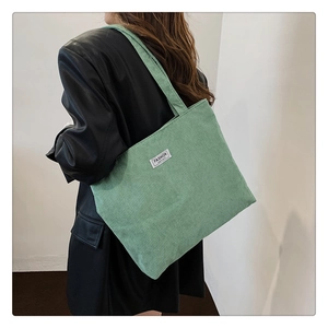Detail view of the green corduroy tote bag worn as a shoulder bag on a model