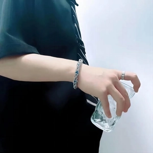 Détail d'un bracelet en chaîne argentée et d'une bague en métal minimaliste porté