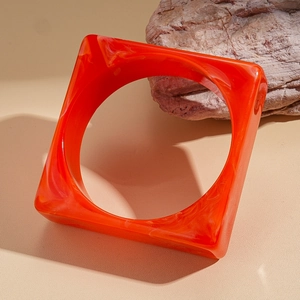 Detail of square orange acrylic bangle with marble texture on natural rock surface