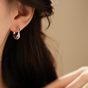 Detailed close-up of a twisted silver hoop earring with sparkling zircon stones