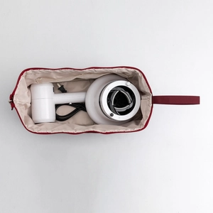 Deep red travel storage bag with compartments holding a hair dryer and accessories