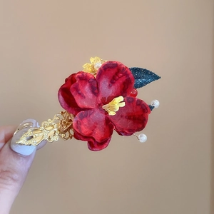 Detailed close-up of a red silk flower hair clip with golden filigree and pearl tassels