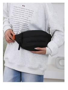 Close-up of black canvas waist bag with embossed letters and orange fashion strap detail