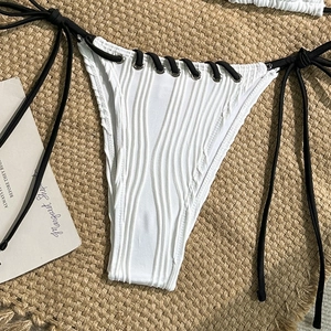 Detail of white ribbed bikini bottom with black side-tie laces and metal eyelets on straw mat